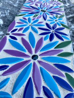 an artisticly designed tile with blue and purple flowers in the center on a marble surface