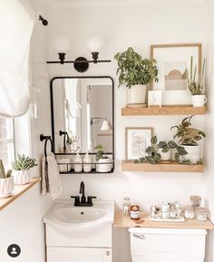 a white bathroom with plants and pictures on the wall above the toilet, along with a sink