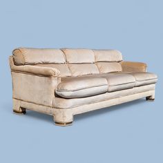 a beige leather couch sitting on top of a blue floor next to a white wall