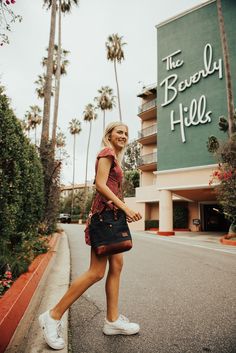 a woman is walking down the street in front of a hotel and smiling at the camera