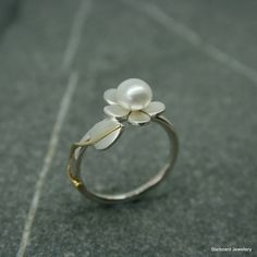 Handcrafted sterling flower ring with single freshwater pearl, created in our own studio In Newlyn, Cornwall The five petal silver daisy measures 11.5 mm which is set with a freshwater pearl and to one side is a leaf with a brass tendril all sitting on a silver band. The freshwater pearl is 6.5mm The silver flower and leaf have a satin finish. UK finger sizes  J to T Other sizes on request  All my designs are hand made and no two are exactly the same. All my jewellery comes in a presentation gift box.  Thank you for your time. Please note that international shipping fees do not include possible custom charges for your country and you will be solely responsible for payment of these charges.  We are required by law to fully disclose the contents and value of the items in your package for Cus Elegant White Flower-shaped Pearl Ring, Delicate Silver Pearl Ring For Anniversary, Bridesmaid Pearl Necklace, Nature Wedding Ring, Silver Jewlery, Wax Ring, Art Nouveau Ring, Single Pearl Necklace, Silver Flower Ring