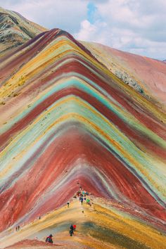 people are walking on the side of a hill covered in multicolored rocks and grass