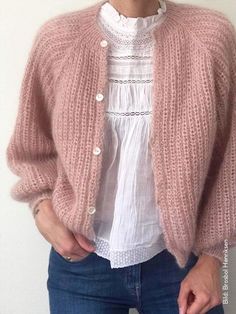 a woman standing in front of a white wall wearing a pink sweater and cardigan