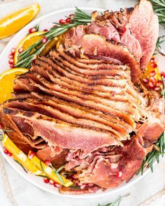 a white plate topped with meat covered in rosemary garnish next to sliced oranges