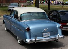 an old blue car is parked on the side of the road in front of other cars