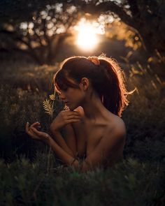 a naked woman sitting in the grass with her hands on her chest and looking down