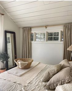 a bed with pillows and a basket on top of it next to a window in a bedroom