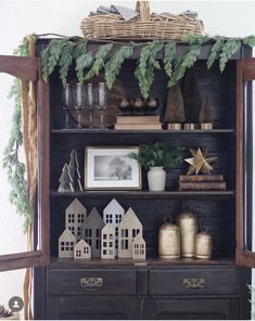 an old bookcase has christmas decorations on it and is decorated with greenery, pine cones, twinklings, and small houses