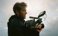 a man holding a camera in front of his face and looking at the sky behind him