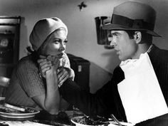 a man and woman standing next to each other in a kitchen eating doughnuts