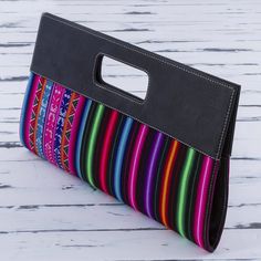 a multicolored purse sitting on top of a wooden table next to a white wall