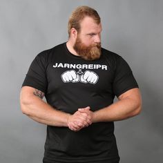 a man with a beard standing in front of a gray background wearing a black shirt