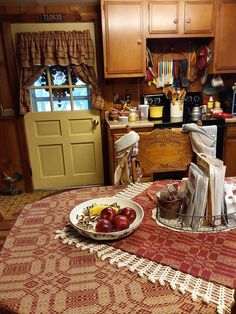 a bowl of fruit on a table in a kitchen with wooden cabinets and an open door