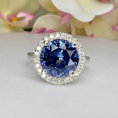 a blue and white diamond ring sitting on top of a table with flowers in the background