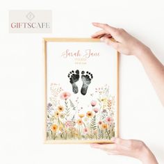 two hands holding up a framed photo with flowers and baby footprints