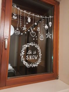 a window with christmas decorations hanging from it's side and the words let it snow written in white