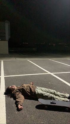 a person laying on the ground next to a skateboard in an empty parking lot