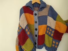 a multicolored knitted sweater hanging on a wooden hanger with a white wall in the background