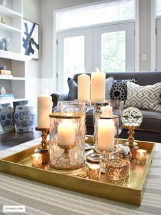 a tray with candles on top of it in front of a couch and coffee table