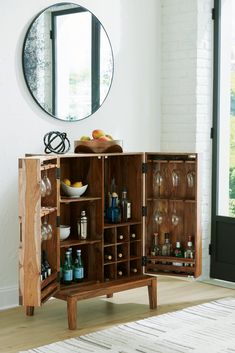 a wooden cabinet with wine glasses and bottles in it next to a round mirror on the wall