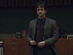 a man wearing a suit and tie standing in front of a dresser with his hands in his pockets