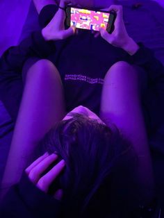 a woman laying on her back holding a cell phone in front of her face and looking at the screen