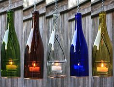 four different colored wine bottles hanging from chains with candles in them and one lit candle inside the bottle