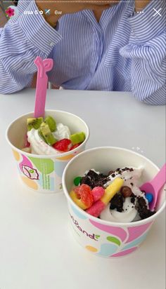 two cups filled with ice cream and fruit on top of a white table next to a stuffed animal