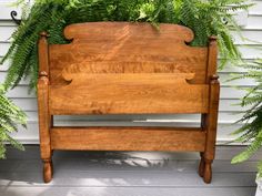 a wooden bed frame sitting on top of a porch next to some green plants in front of a house