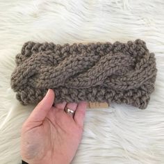 a hand is holding up a gray knitted headband