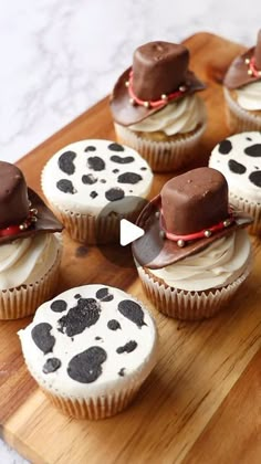 several cupcakes with chocolate hats on them sitting on a cutting board next to each other