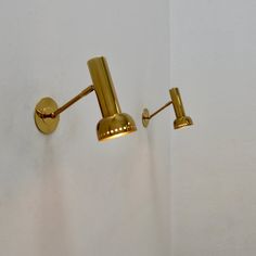 two brass wall lights on the side of a white wall