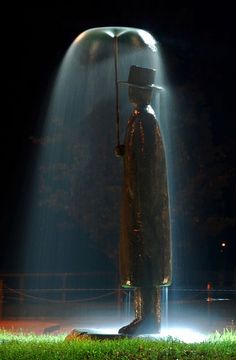 a man with a hat and cane standing in front of a water fountain at night