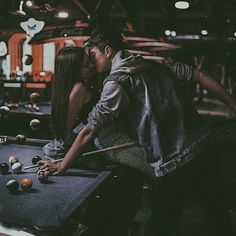 two people are kissing while playing pool in a dark room with many balls on the table