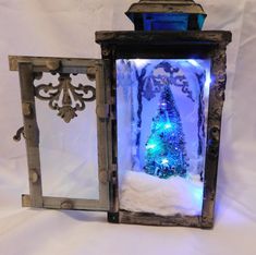 a small christmas tree in a glass box with snow on the bottom and an old fashioned mirror behind it