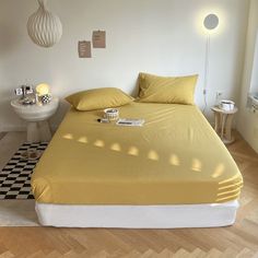 a bed with yellow sheets and pillows in a white room next to a checkered floor