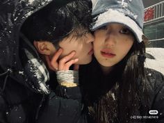 two people are kissing in the snow with one person wearing a hat and holding his hand to his face