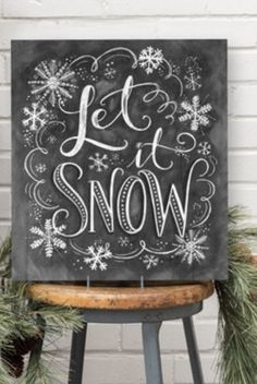 a chalkboard sign that says let it snow on top of a stool next to pine branches