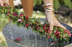 a woman is sprinkling water from a bucket filled with flowers and greenery