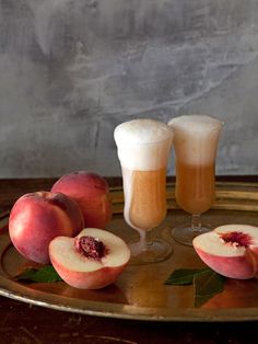 two glasses and three pieces of fruit sitting on a gold platter next to each other