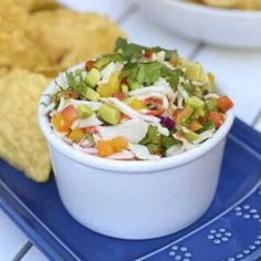 a white bowl filled with salad sitting on top of a blue plate next to chips