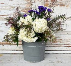 white and purple flowers are in a gray bucket