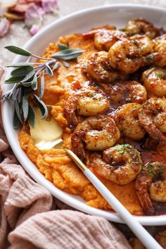 a white bowl filled with mashed potatoes topped with cooked shrimp and garnished with herbs