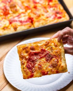 a slice of pizza is being held up by someone's hand on a paper plate