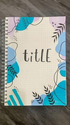 a spiral notebook with the word title written in black ink on top of a blue and pink flowered background