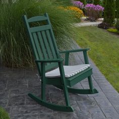 a green rocking chair sitting on top of a stone walkway next to grass and flowers