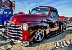 an old red truck parked next to another blue truck at a car and motorcycle show