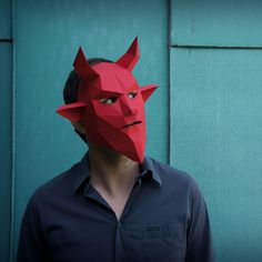 a man wearing a red paper mask with horns on his head, standing in front of a green wall