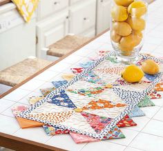 a glass vase filled with lemons sitting on top of a kitchen counter next to a table