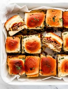 a white tray filled with mini sandwiches covered in cheese and tomato sauce, on top of a marble countertop